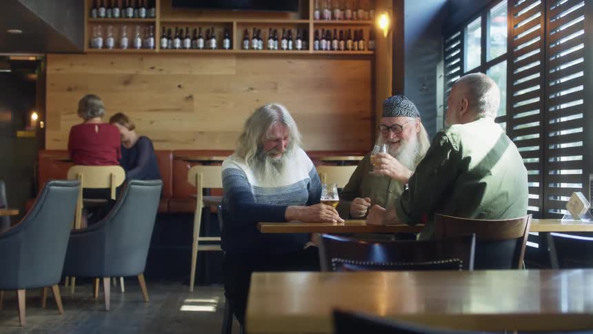 A trio of men sit together while talking and laughing over a few glasses of beer