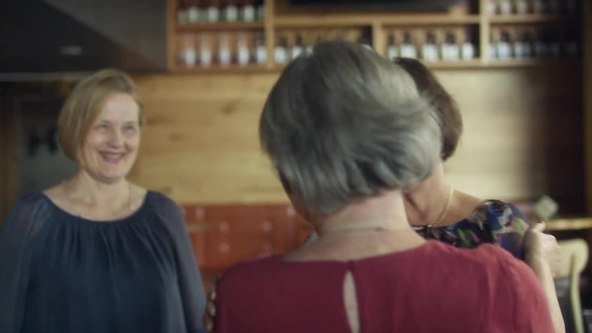 Group of elderly friends greeting each other with hugs inside a restaurant