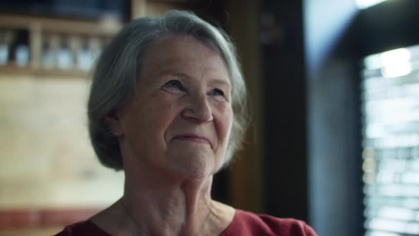 Elderly woman standing inside a bar looking up smiling