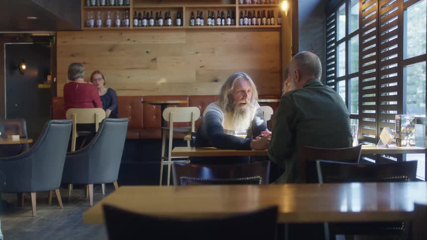 Old friends sit at restaurant table together reaching out to clasp hands