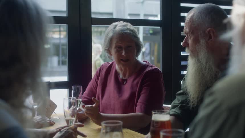 A woman and men with long white beards chat over drinks at a restaurant