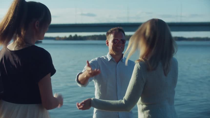 Friends hug each other in greeting on edge of water with traffic flowing across bridge in background