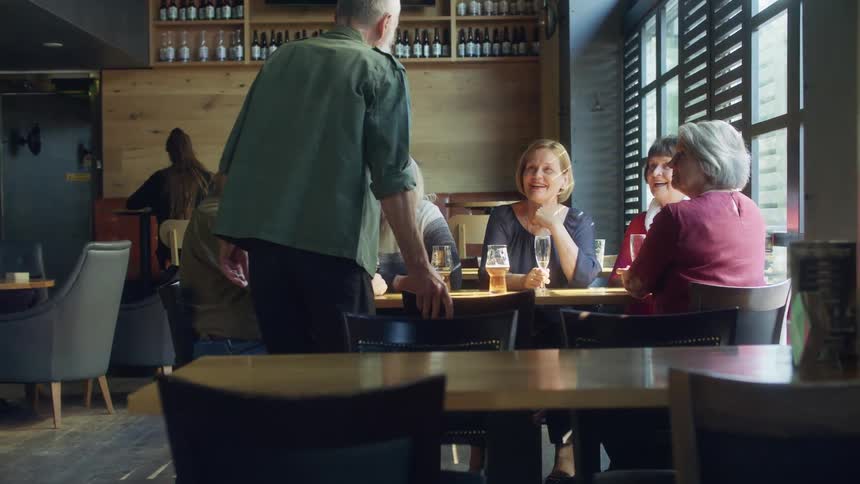 Five people are talking and drinking at a table as another man joins them