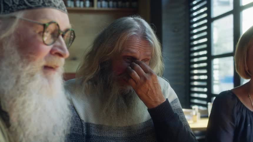 Older friends sit around table in restaurant laughing and talking
