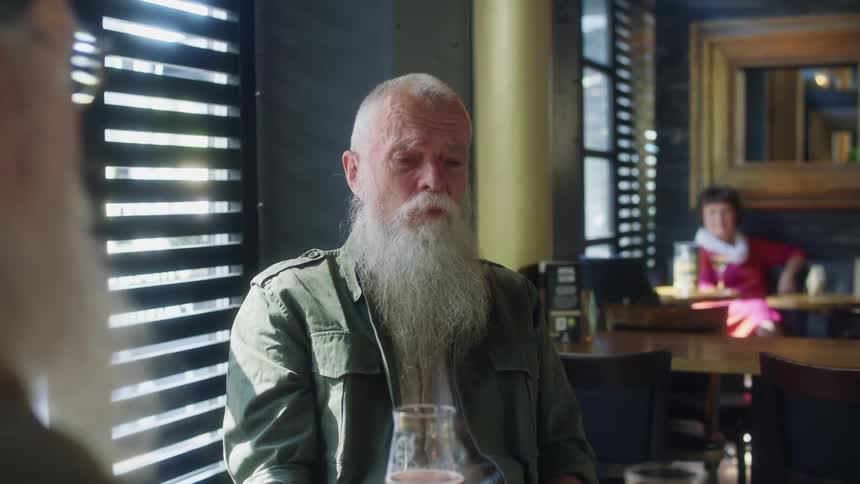 Elderly men with long beard sit at table and talk with each other in pub