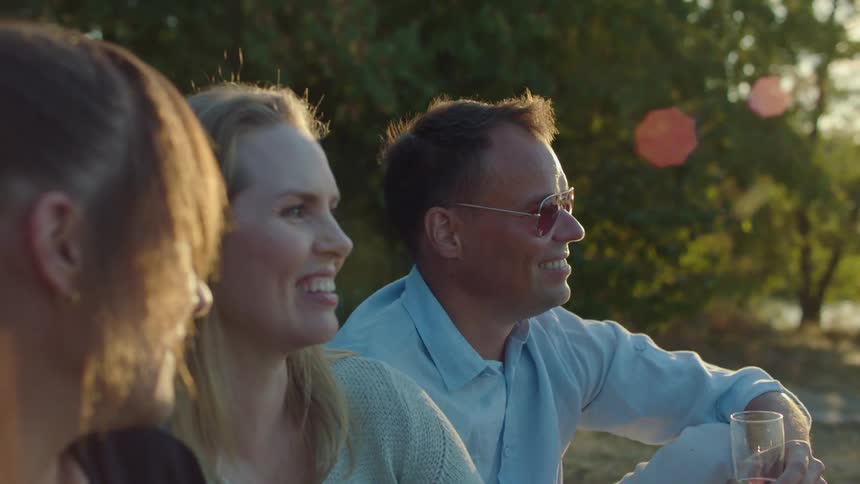 Group of friends sitting outdoors talking while drinking champagne at sunset