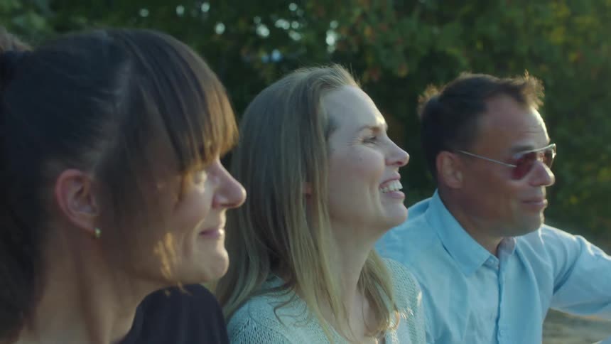 Three people are sitting outdoors as they are drinking and talking to each other