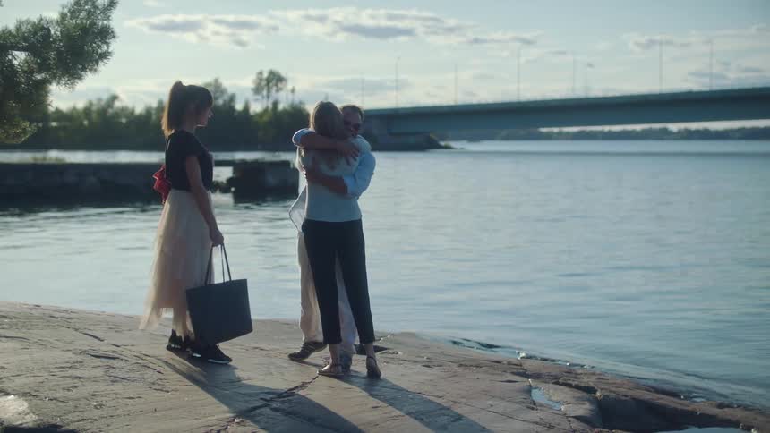 Three people greet and hug by the water