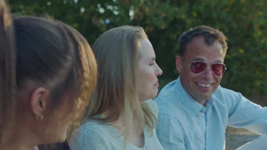 Friends sit on ground with wine bottle talking and smiling