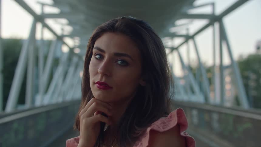 Fashion model poses on bridge with city buildings in background