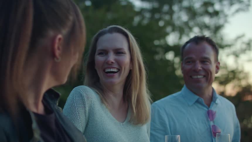 A group of middle aged people chat outdoors while drinking wine