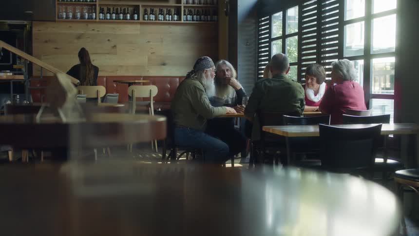 A group of elderly women and bearded men crowd around a small table in a restaurant