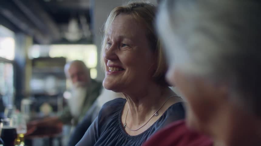 A group of elderly men and women sits at table talking with each other in bar