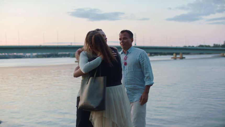 A woman hugs another woman and a man as they say good bye and walk away