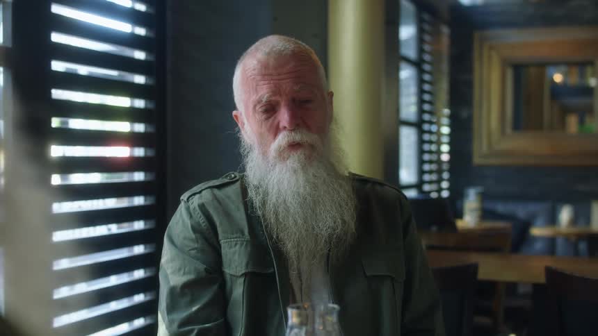 Man comforts another elderly bearded man as friends sit talking at table in restaurant