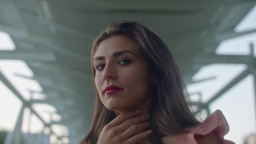 A woman looks at the camera as she touches her face and hair