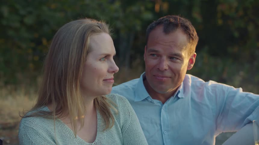 A man smiles at a woman as they sit outside