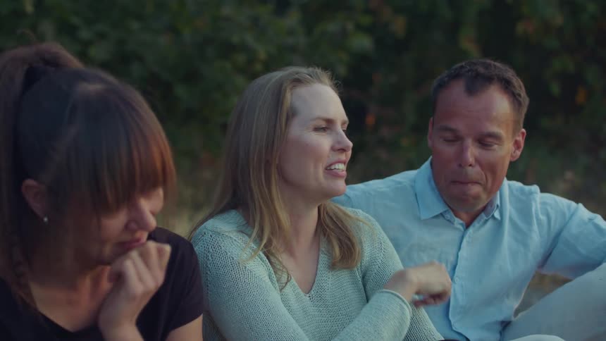 Three people laugh together as they sit outside