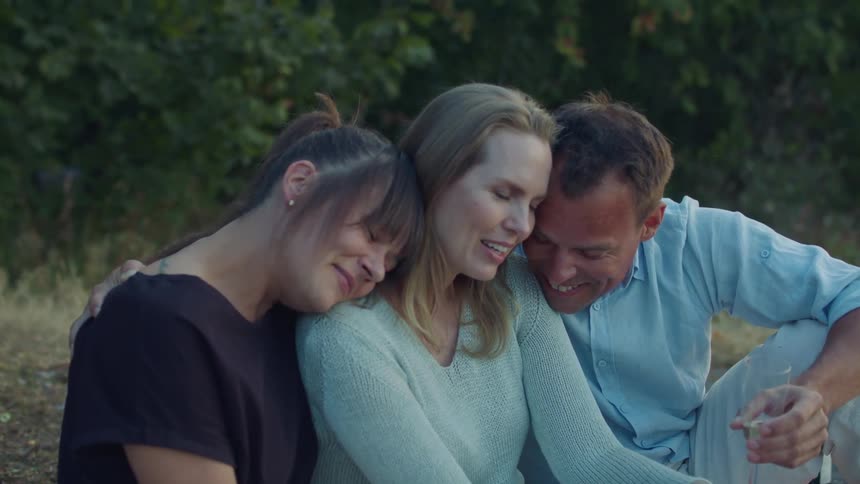 Group of friends sitting on a field holding champagne glasses hug each other