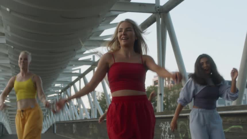 A group of women dance together on a bridge in a city during the day