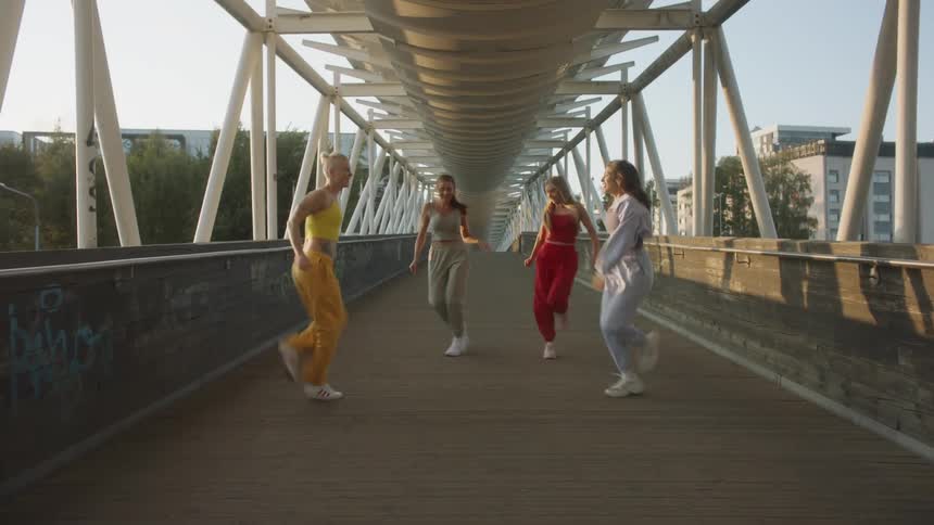 Young friends dancing energetically over a bridge on the city at sunset