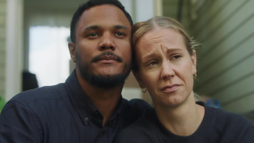 A man comforts a sad woman as they sit next to a building