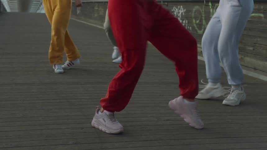 Female dancers dance on wooden slats of pedestrian bridge decorated with graffiti