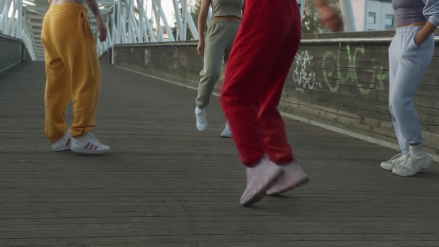 A group of women in track pants dance together on a bridge in a city during the day