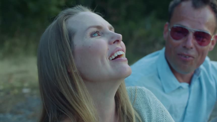 A group of people talk and laugh together while sitting outdoors in a field during the day