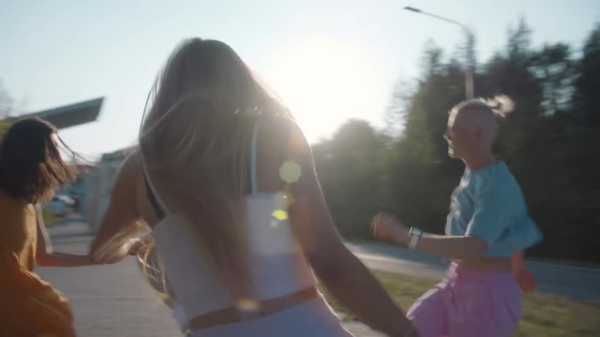 Group of friends energetically dancing under a bridge near a park at sunset