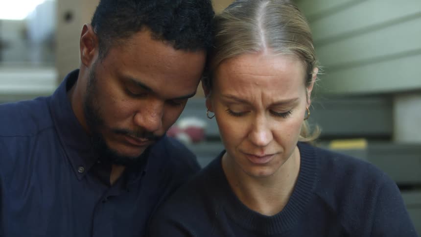 A man and a woman hugging and crying with a baby in the foreground