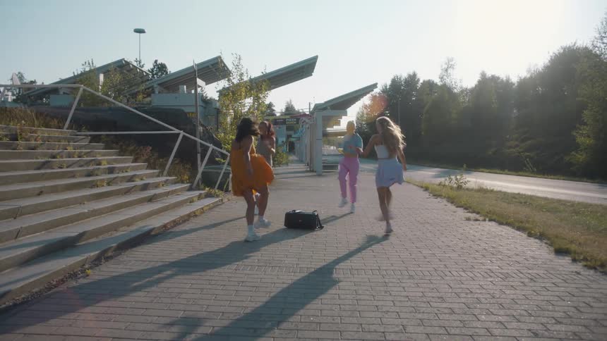 Female dancers dance around boombox on brick path between stairs and road