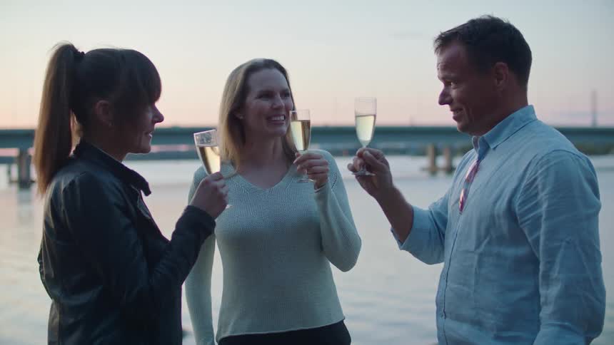 Group of friends standing near a lake at sunset talking and drinking champagne