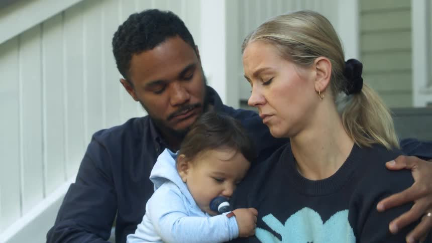 A father sits down next to his wife with a baby