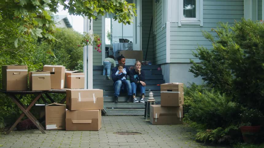 Family sitting down on the stairs in the porch at home in front of cardboard boxes while moving