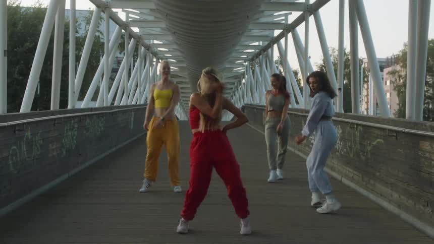 Group of woman wearing bright colored clothes dancing over a bridge near the city at evening
