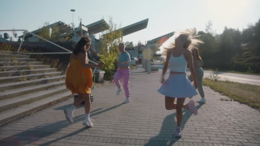 A group of four young women happily dance together while outside on a sunny day