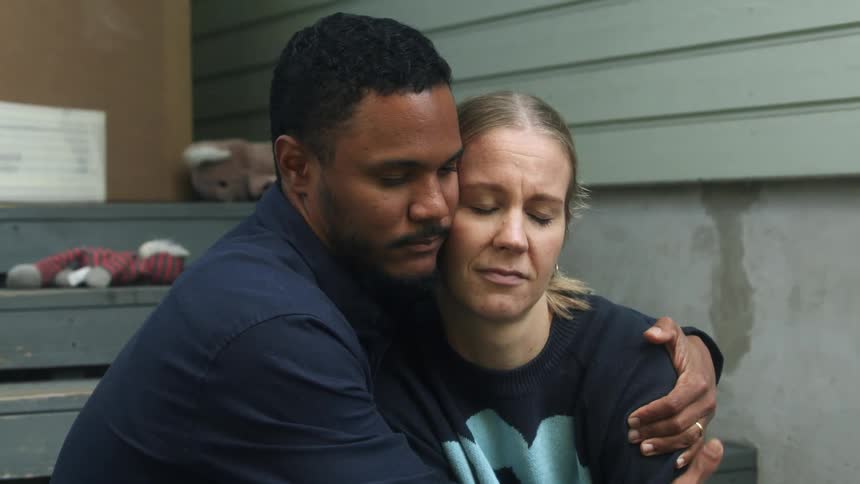 A man hugs and comforts a troubled woman while sitting outdoors on the steps of a home
