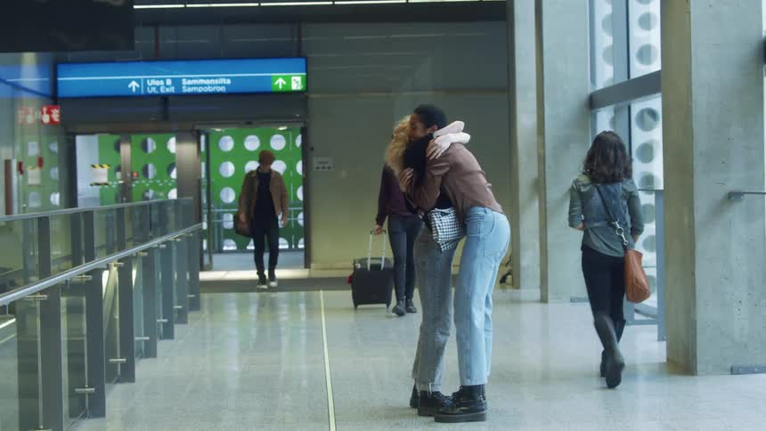 Young friends greet each other with hugs inside a passenger terminal