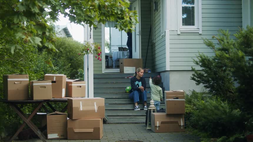 Man walks down steps to pick up baby just after mom sitting with another child and several cardboard boxes kissed the baby
