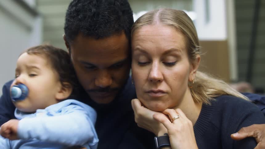 A man holding a baby sits down to comfort a woman
