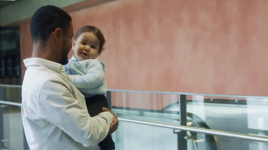 Man standing near escalators holding a small child on his arms