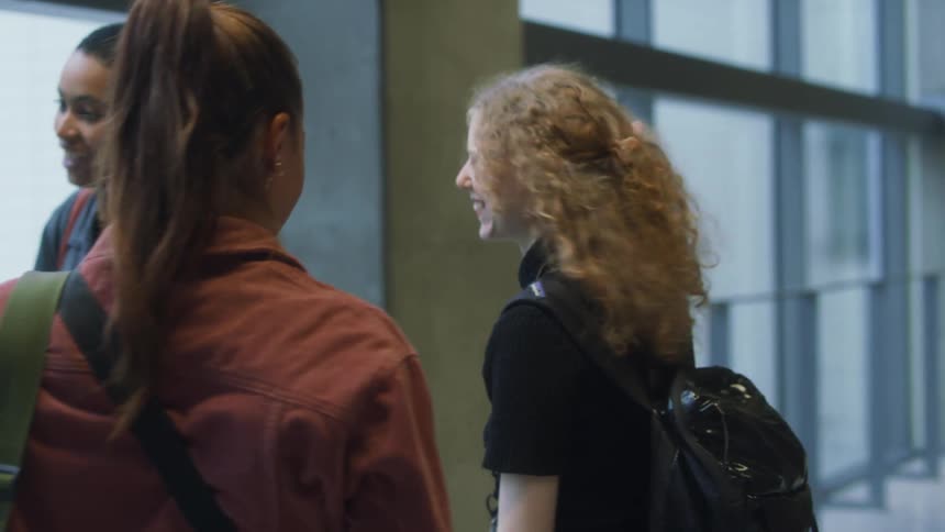 Four female friends greet each other with smiles and hugs standing in building near floor to ceiling mirrors