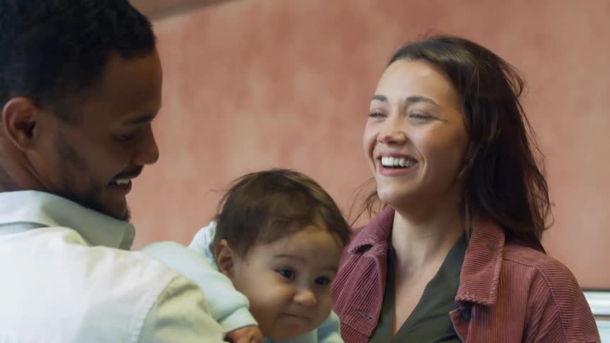 A woman and man holding a baby are having a happy conversation outdoors during the day