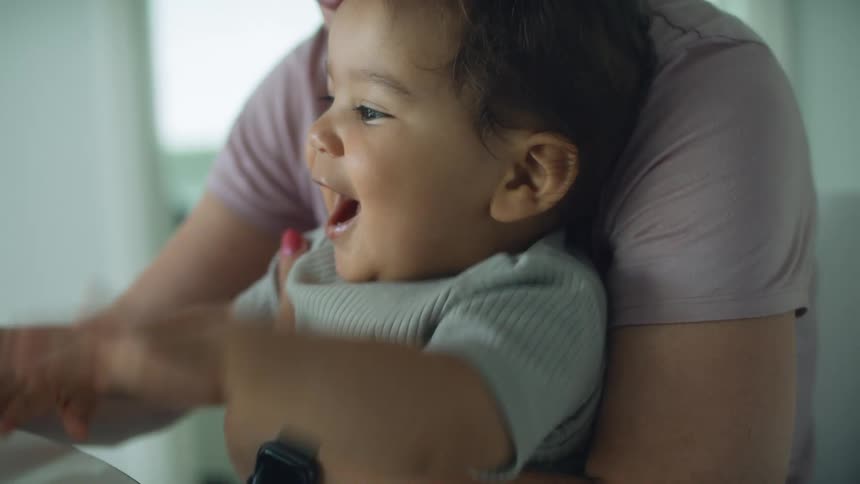 Toddler boy sits on blonde moms lap making a video call on laptop