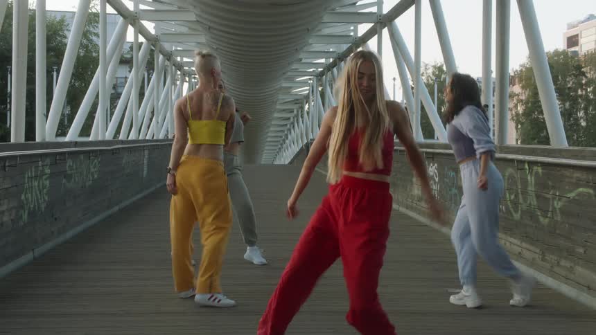 Group of woman wearing bright colored clothes dancing over a bridge near the city at evening