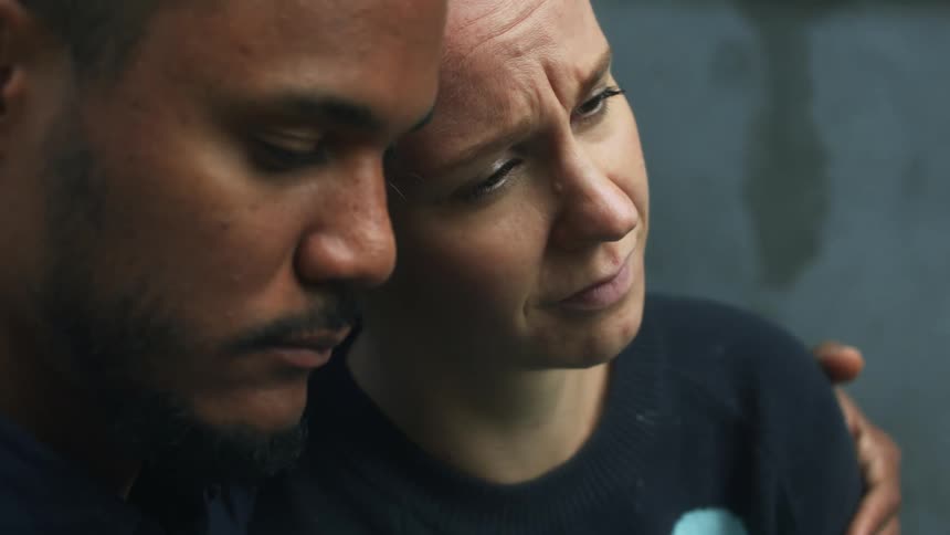 Man hugs and kisses a sad crying woman on the forehead while sitting together