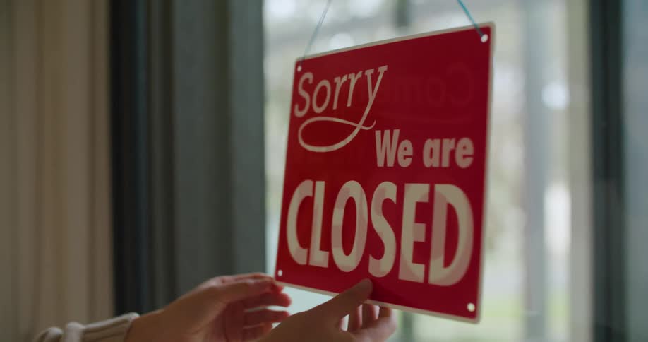 Woman wearing sweater flips sign from closed to open in window