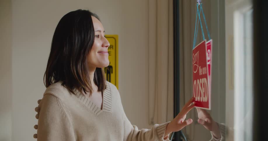 A woman smiles as she flips the sign on the door to open