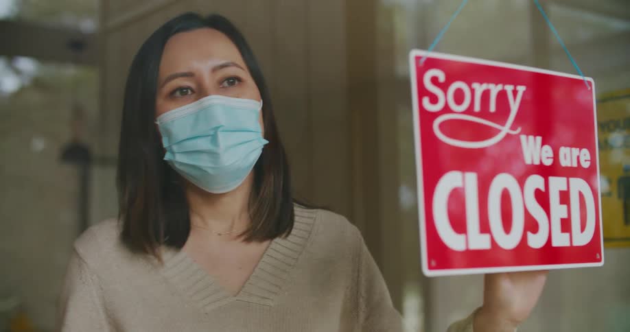 A woman wearing a mask flips the store sign from open to closed